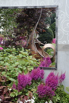 Hampton Court Flowershow 2009, The Sadolin Nature to Nuture Garden designed by Philippa Pearson.  Astilbe chinensis 'Vision in Red' growing beside metal sculpture reflected in mirror behind.