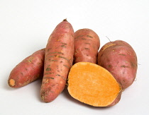 Group shot of Sweet potato, Ipomoea batatas on a white background with one potato cut in half to show the orange interior.