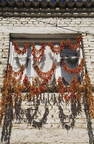 Turkey, Aydin Province, Kusadasi, Strings of red and orange chilies hung up to dry in late afternoon summer sunshine across windows of whitewashed house in the old town casting shadows over the brickw...