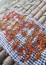 Turkey, Aydin Province, Sirince, Red and orange chilies laid out to dry in late afternoon sun on checked cloth spread over tiled rooftops of house in the old town.