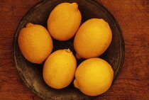 Lemon. Studio shot from above of five lemons on tin or pewter plate on wooden board.