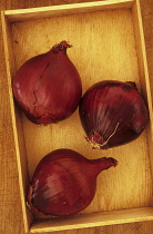 Onion, Allium cepa 'Red Baron'. Studio shot of three red onion lying in wooden tray on wood board.