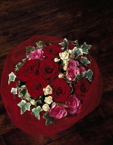 Rose, Rosa 'Passion',Overhead view of a bouquet of six red roses with six pink and white roses with variegated ivy, surrounded by a red net wrap.