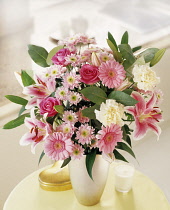 Lily, Lilium 'Star Gazer', Floral arrangement with pink chrysanthemum roses and carnations in a vase on a small table.