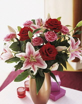 Lily, Lilium 'Star Gazer', Floral arrangement with pink and red roses in a vase on a small table.