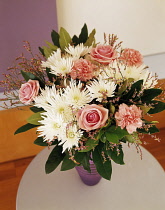 Daisy, White Chrysanthemum,  pink roses and carnations, fFloral arrangment with greenery in a vase on a small wooden table.