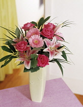Lily, Lilium 'Star Gazer', Floral arrangment with pink roses and Gerberas in a vase on a small table.