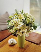 Lily, Lilium 'Star Gazer' white form, Floral arrangement with white chrysantemum and green carnations arranged in a vase on a small table.