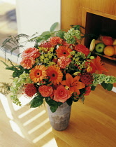 Carnation, Dianthus, Floral arrangment  with Gerberas, Oriental Lilies and Bells of Ireland in a vase on a wooden floor.