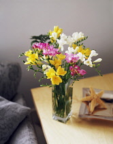 Freesia, Floral arrengment of pink, white and yellow flowers in a glass vase on a small wooden table.