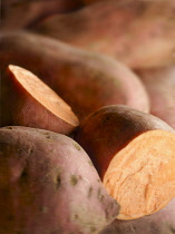 Sweet potato, Ipomoea batatas, Several potatoes with one cut open to reveal pale orange flesh.