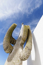 Saguaro cactus, Carnegiea gigantea, Dramatic view from below of a single stem with arms branching upwards towards a blue sky with wispy clouds, its shadow on a white wall.