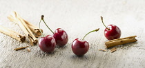 Cherry, Prunus cultivar. Four cherries with stalks arranged with broken pieces of cinnamon sticks on light coloured ditressed wood background.