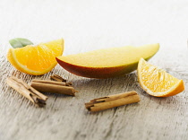 Mango, Mangifera indica. One slice arranged with quarters of orange and broken pieces of cinnamon stick on pale, distressed, wooden background. Selective focus.