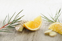 Ginger, Zingiber officinale root arranged with sprigs of Redbush or Rooibus, Aspalathus linearis and pieces of orange on pale, distressed, wooden background. Selective focus.