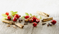 Rosehip, Rosa canina. Several hips arranged with leaves and pieces of cinnamon stick and cloves on pale, distressed, wooden background. Selective focus.