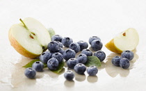 Blueberry, Vaccinium corymbosum cultivar. Several berries with a half and quarter of apple and spritzed with water arranged on white marble. Selective focus.