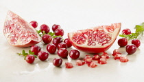 Cranberry, Vaccinium oxycoccos, several berries with leaves and with two pomegranate quarters, spritzed with water, arranged on white marble. Selective focus.