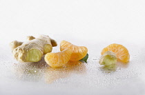 Ginger, Zingiber officinale root with Mandarin, Citrus reticulata, pieces arranged on silver background, and spritzed with water. Selective focus.