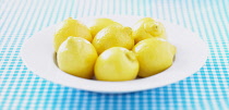 Lemon, Citrus limon, Mass of yellow coloured fruit in white bowl.