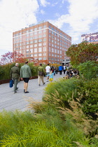 USA, New York, Manhattan, people walking along a path beside plants in autumn colours leading to the Chelsea Market Passage on the High Line linear park on a disused elevated railroad spur called the...
